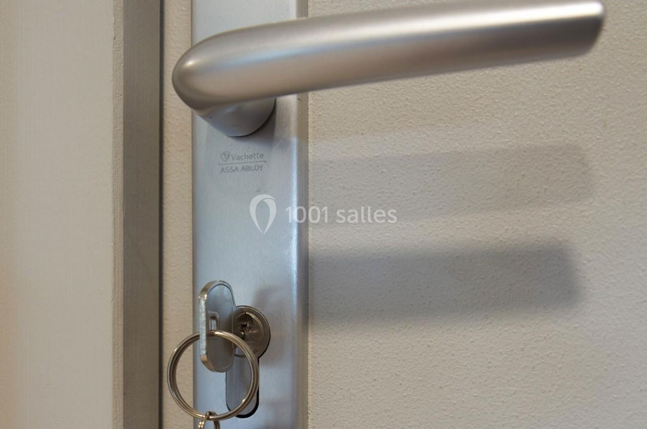 Clé insérée dans une serrure avec poignée métallique sur une porte beige.