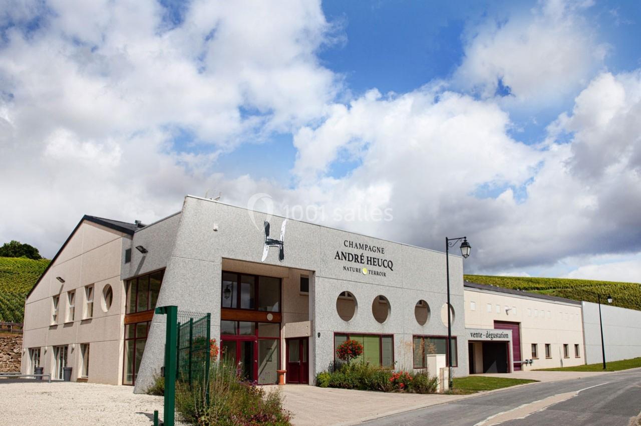 Bâtiment moderne d'une maison de champagne avec façade grise, entouré de vignes sous un ciel partiellement nuageux.