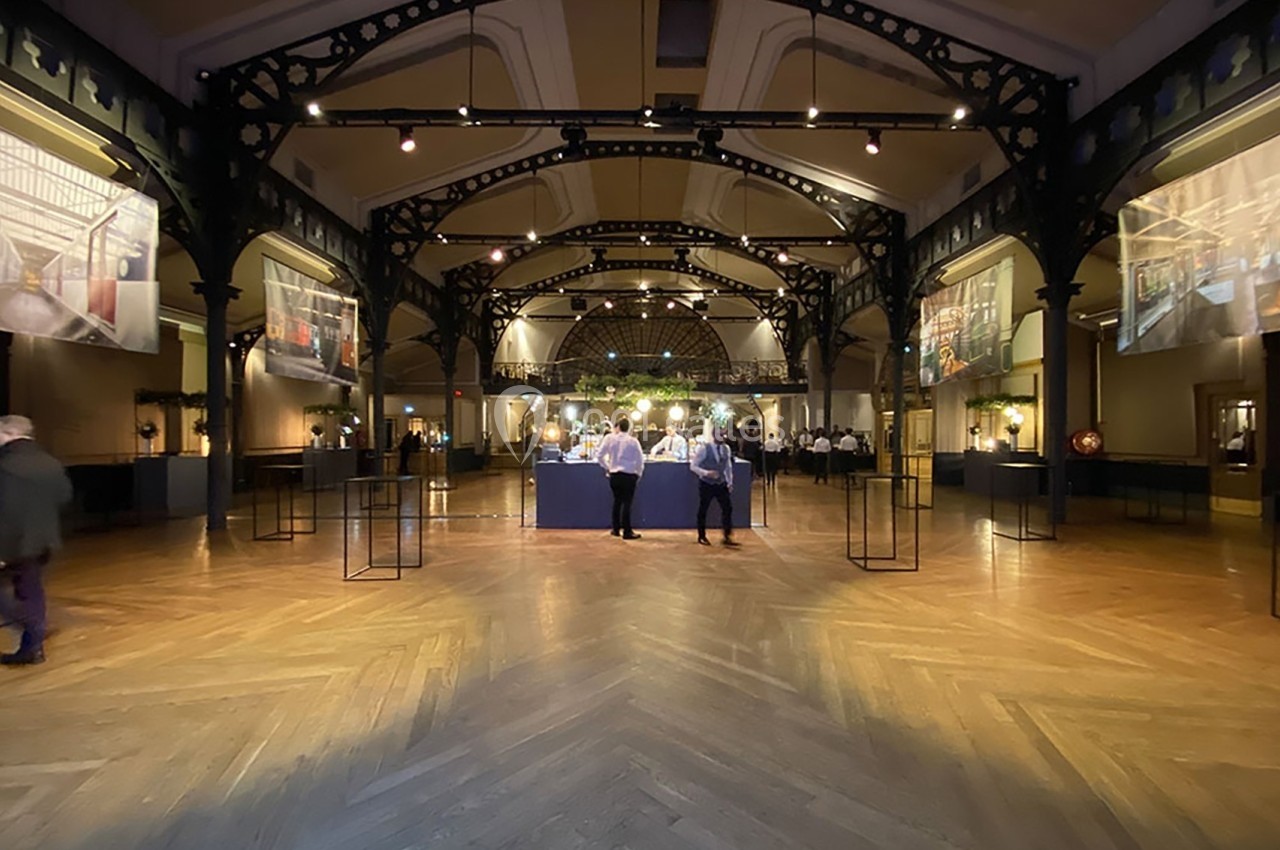 Salle spacieuse avec un parquet en bois, des structures métalliques et un éclairage tamisé, décorée pour un événement.