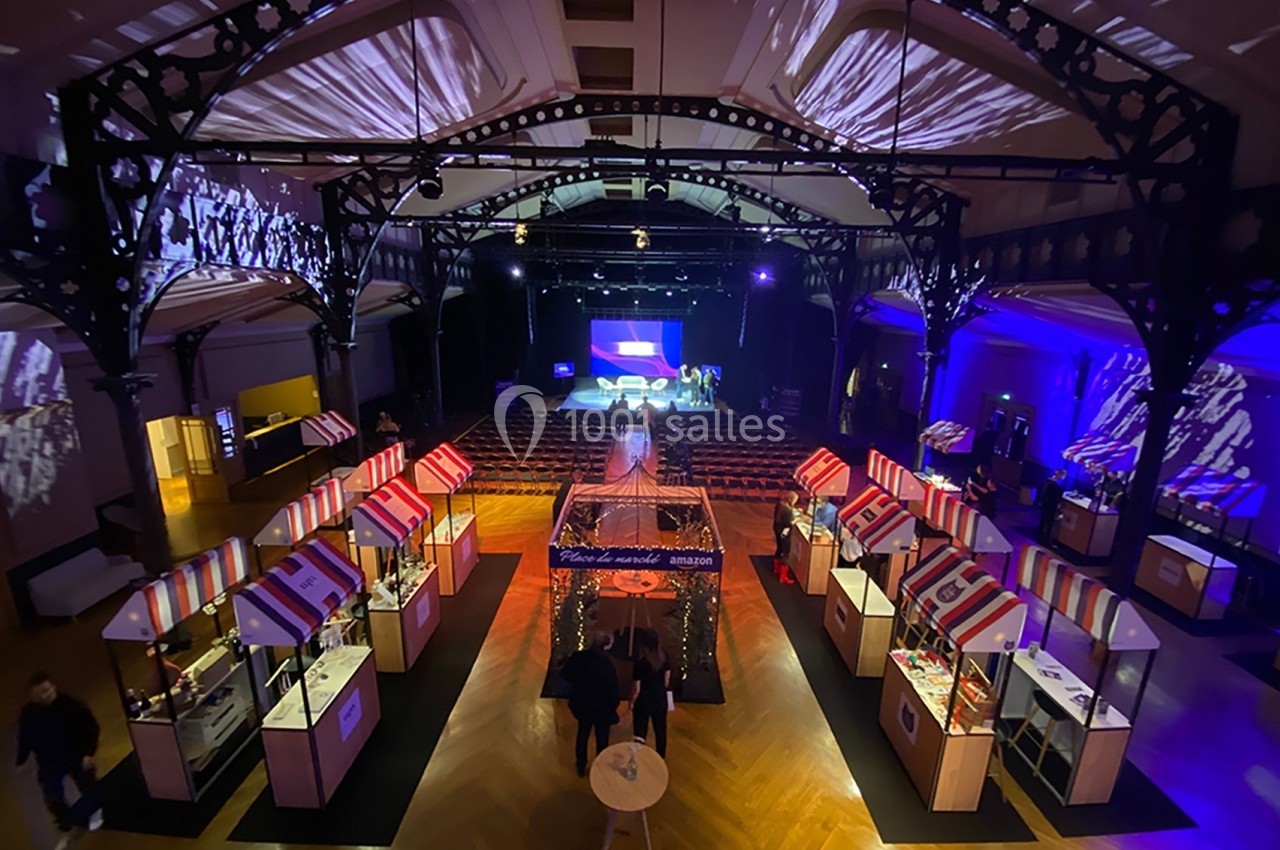 Vue d'une salle événementielle avec des stands colorés, un éclairage tamisé et une scène au fond.