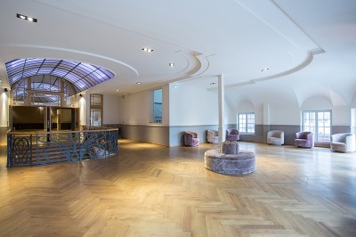 Salle intérieure avec mezzanine, escaliers symétriques, balustrades en métal décoratif et parquet au sol.