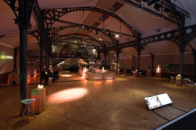 Salle intérieure avec mezzanine, escaliers symétriques, balustrades en métal décoratif et parquet au sol.