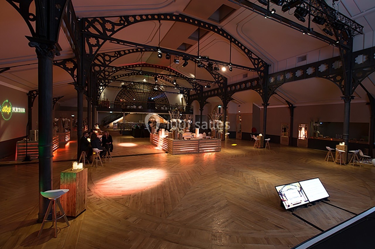 Salle spacieuse avec structure métallique, parquet en bois, éclairage chaleureux et espace aménagé pour un événement.
