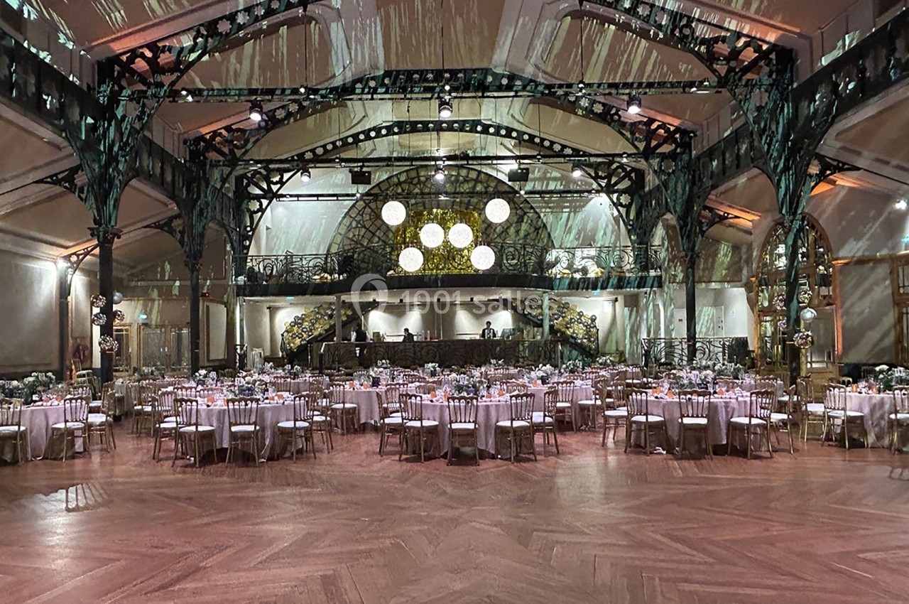 Salle de réception élégante avec tables rondes dressées, éclairage tamisé et architecture métallique ornée.