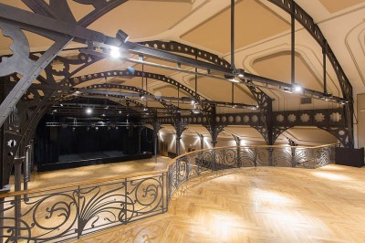 Salle intérieure avec mezzanine, escaliers symétriques, balustrades en métal décoratif et parquet au sol.