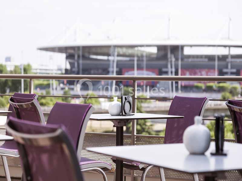 Terrasse avec tables et chaises violettes, vue sur un grand stade en arrière-plan par temps clair.