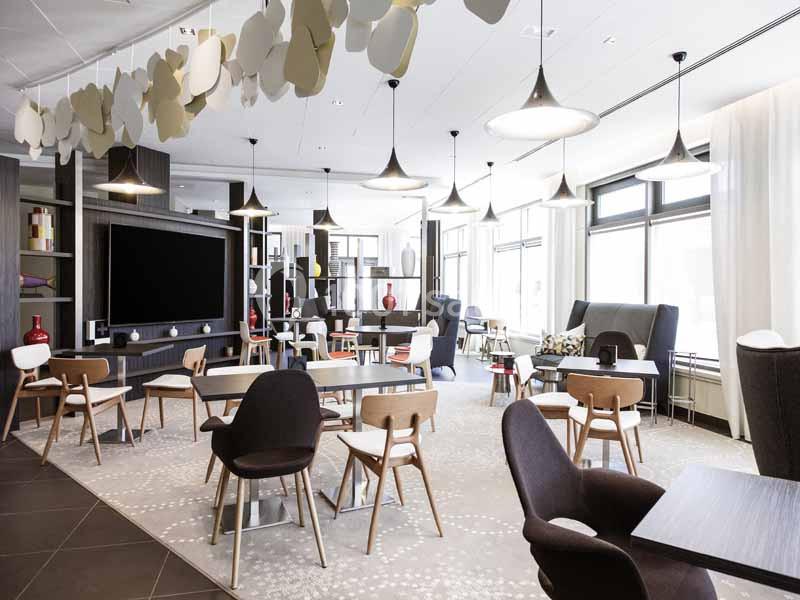 Salle lumineuse avec tables, chaises modernes, luminaires suspendus et décorations murales en forme de feuilles.