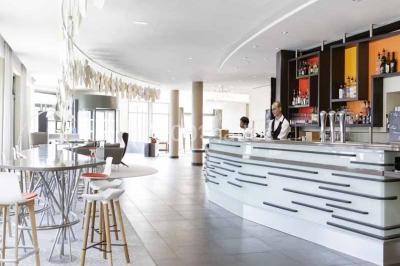Salle de restaurant moderne avec tables dressées, chaises colorées, suspensions lumineuses et grandes baies vitrées.