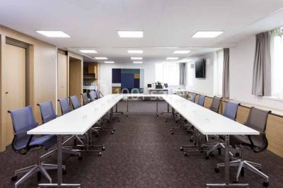 Salle de restaurant moderne avec tables dressées, chaises colorées, suspensions lumineuses et grandes baies vitrées.