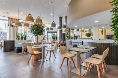 Salle de restaurant moderne avec tables dressées, chaises colorées, suspensions lumineuses et grandes baies vitrées.