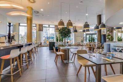 Salle de restaurant moderne avec tables dressées, chaises colorées, suspensions lumineuses et grandes baies vitrées.