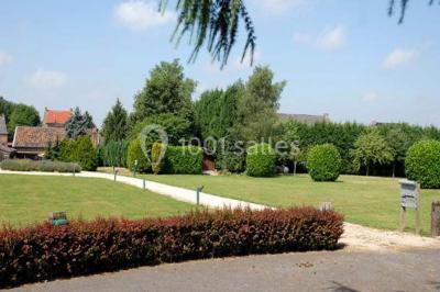 Salle de réception avec tables dressées, nappes beiges, chandeliers et poutres apparentes sous un toit vitré.