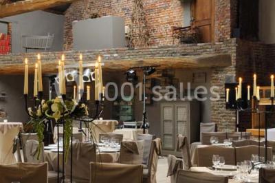 Salle de réception avec tables dressées, nappes beiges, chandeliers et poutres apparentes sous un toit vitré.