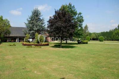 Table et chaises en métal sur une terrasse en dalles, devant un mur blanc avec une porte en bois et des plantes décoratives.
