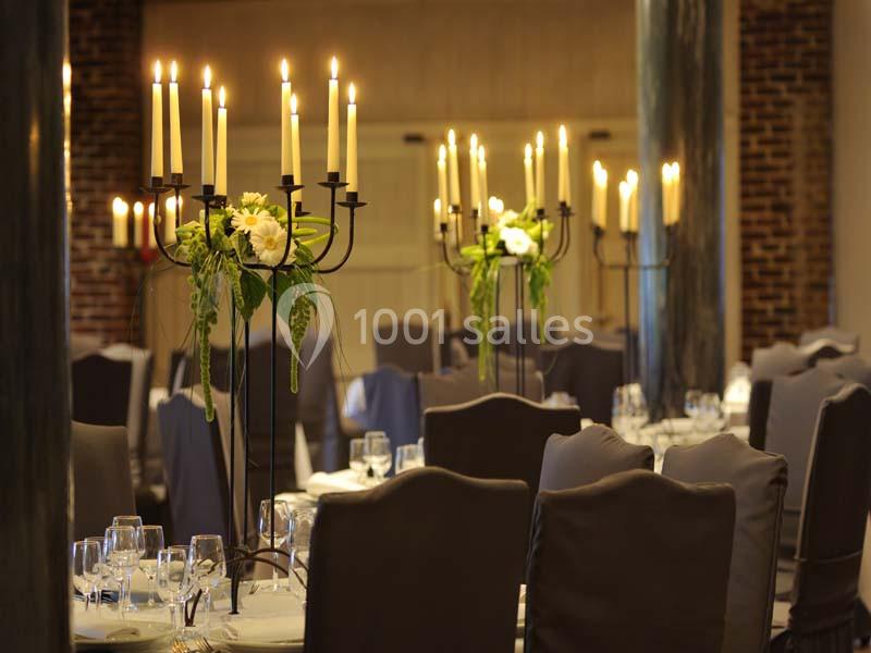 Salle de réception élégante avec tables dressées, chandeliers ornés de fleurs blanches et lumière tamisée.