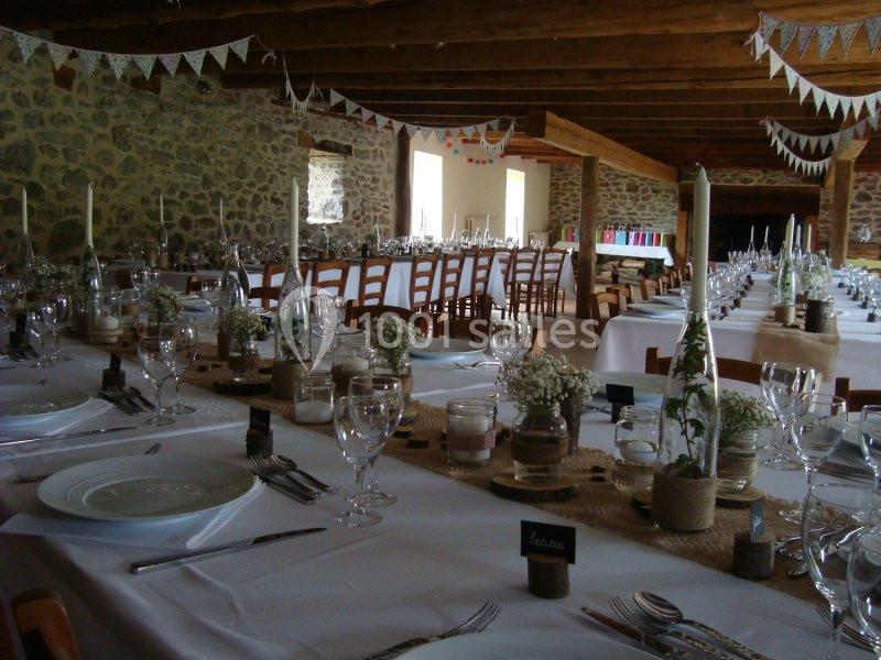 Salle de réception décorée avec des tables dressées, nappes blanches, fleurs et guirlandes suspendues.