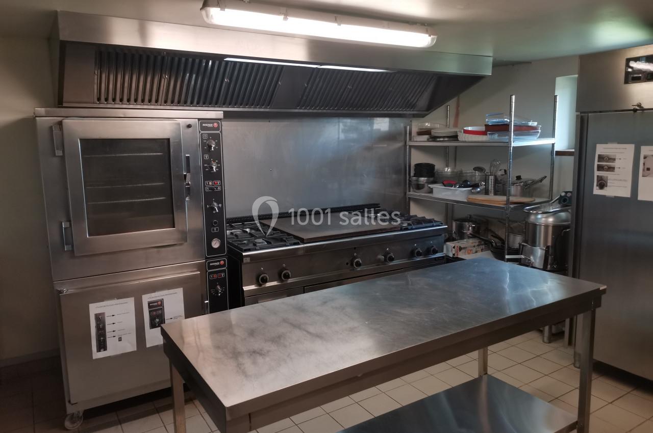 Cuisine professionnelle équipée d'un four, d'une plaque de cuisson, d'une hotte et d'un plan de travail en inox.