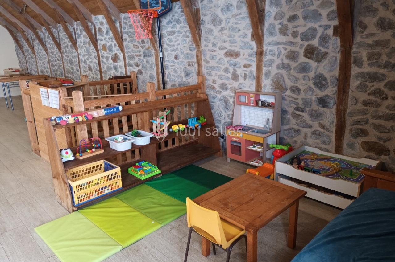 Espace de jeux pour enfants avec tapis colorés, jouets en bois, cuisine miniature et panier de basket dans une salle en…