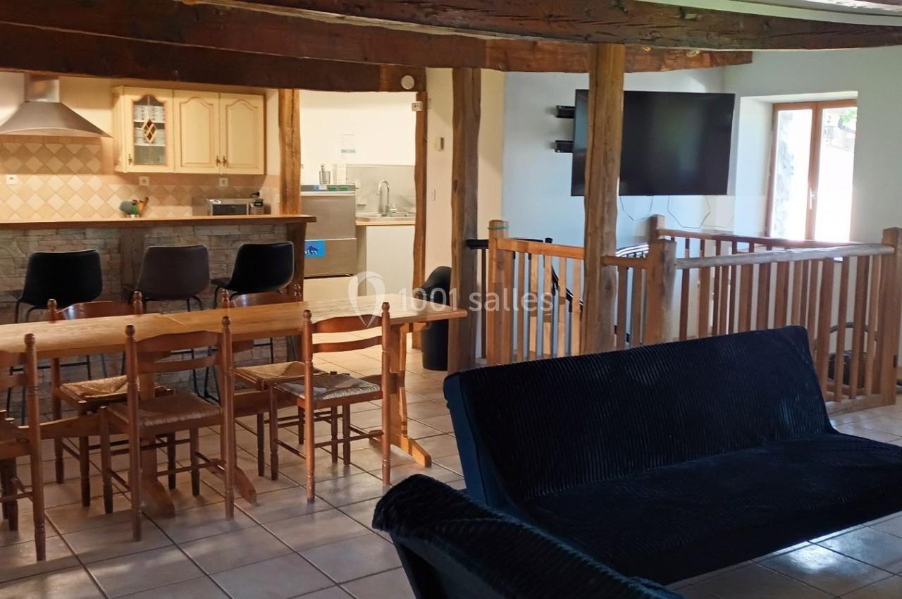 Salle à manger ouverte avec table en bois, cuisine équipée au fond, salon avec canapés et télévision à droite.