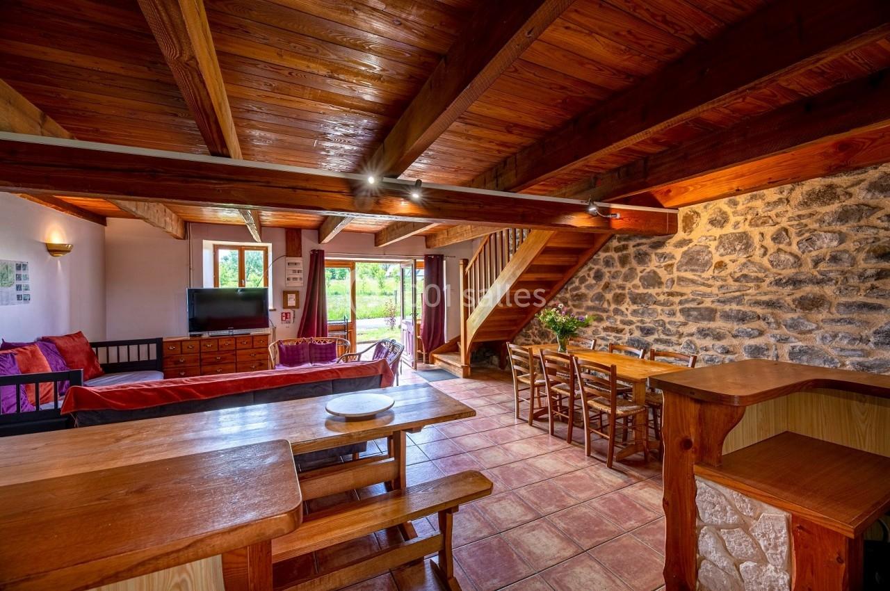 Salle de séjour rustique avec poutres en bois, murs en pierre, table à manger et coin salon lumineux.