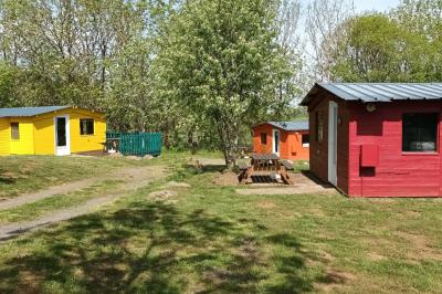 Trois petits chalets colorés en bois, entourés d'arbres et de pelouse, sous un ciel dégagé.