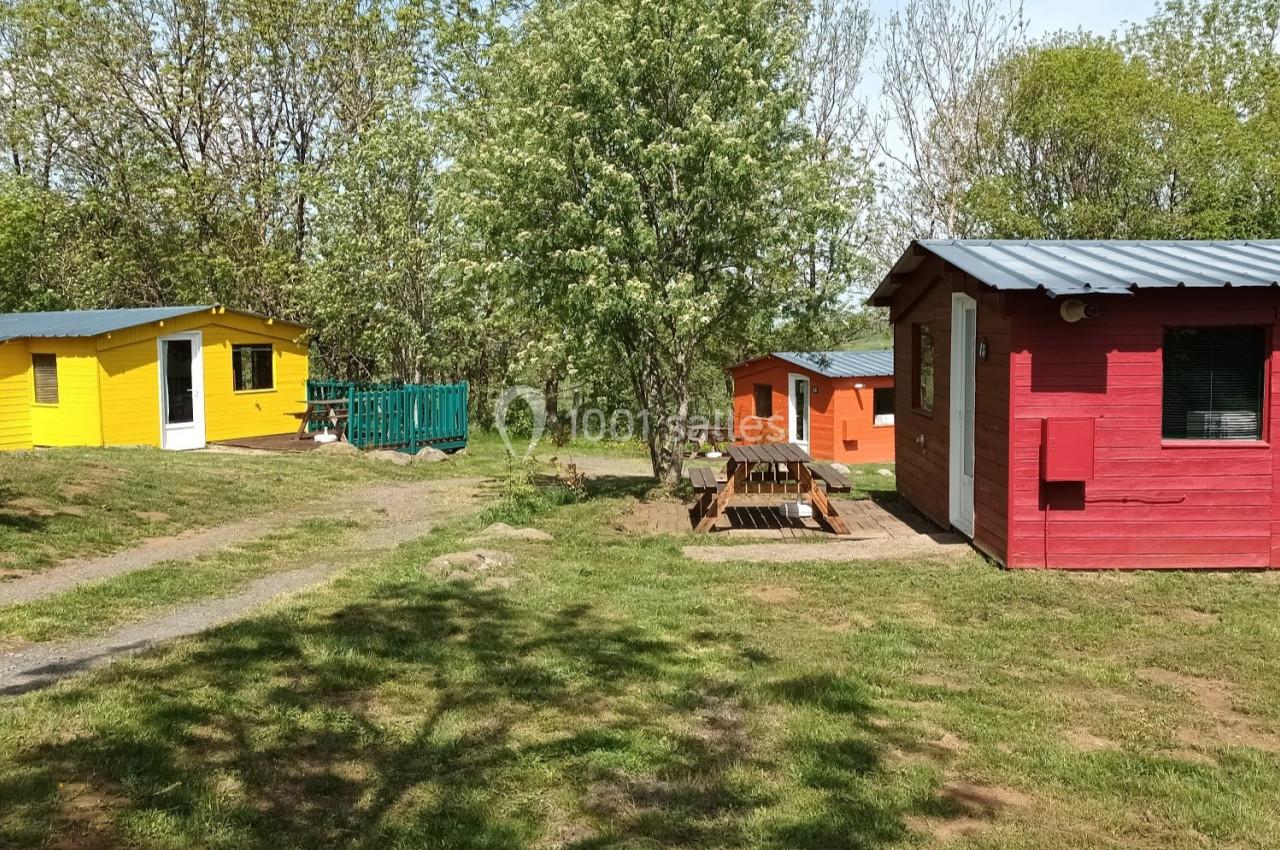 Trois petits chalets colorés en bois, entourés d'arbres et de pelouse, sous un ciel dégagé.