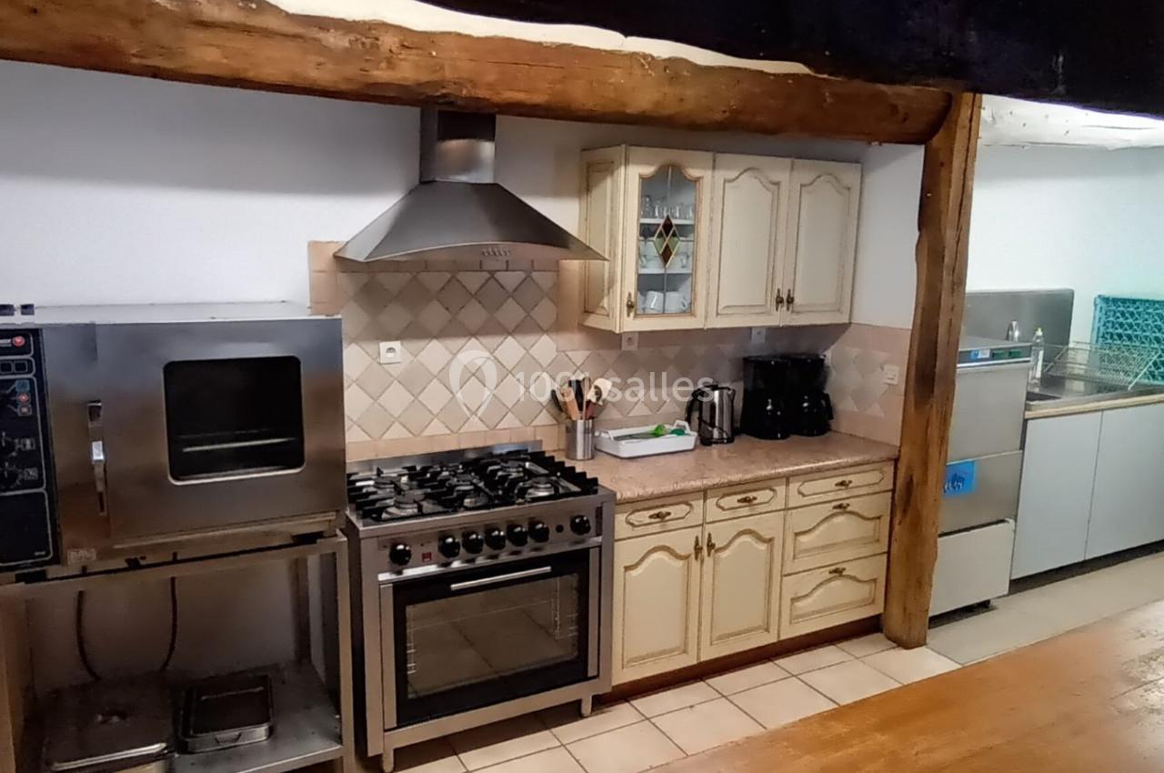 Cuisine équipée avec four professionnel, cuisinière, hotte, évier, lave-vaisselle et meubles en bois clair.