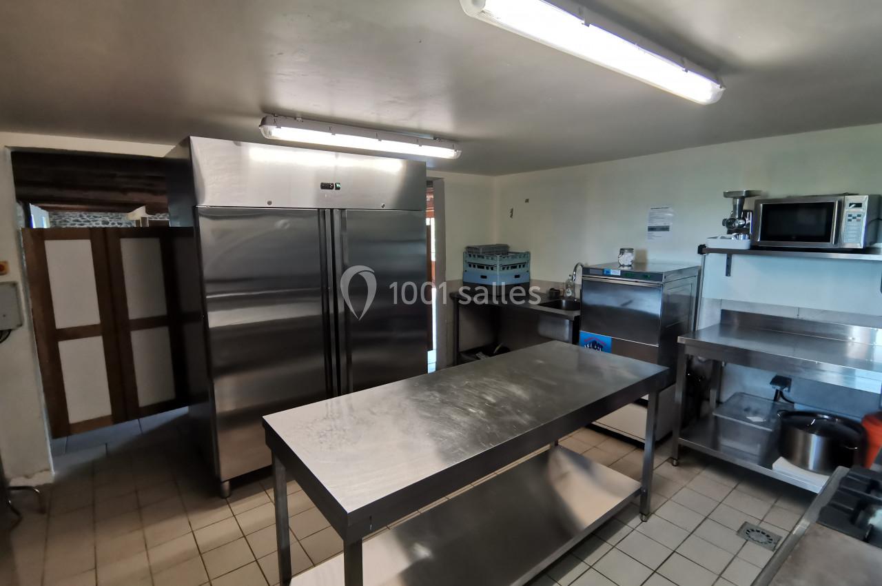 Cuisine professionnelle équipée avec plan de travail en inox, réfrigérateurs, micro-ondes et équipements divers.