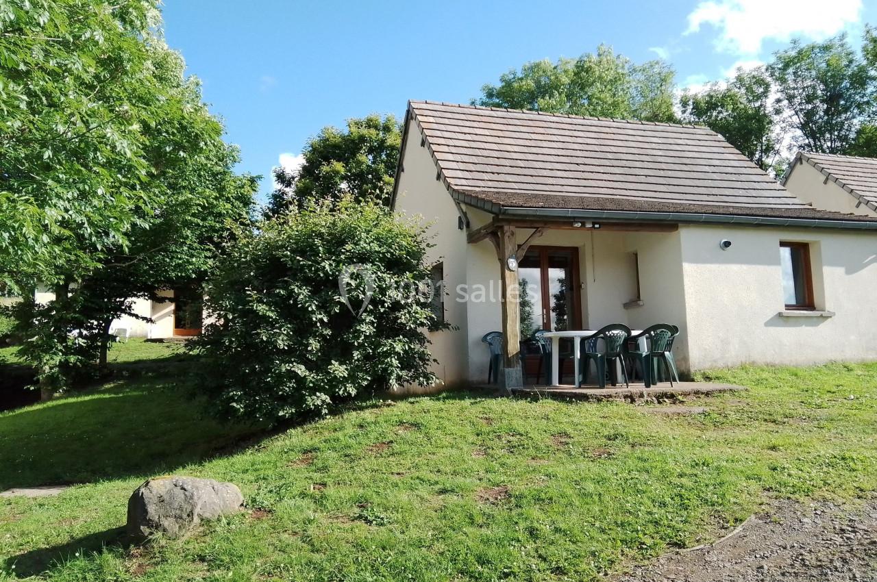 Maison individuelle avec terrasse, entourée de verdure et arbres, sous un ciel bleu partiellement nuageux.