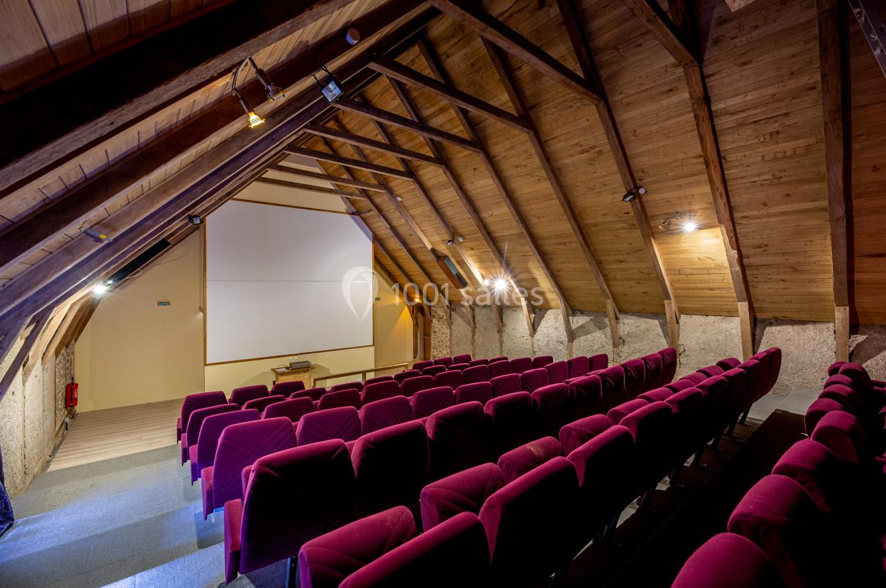 Salle de projection sous un toit en bois avec des rangées de fauteuils rouges et un écran blanc.