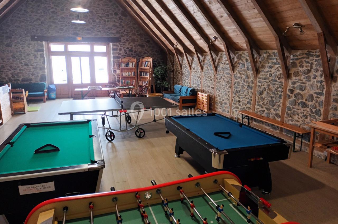 Salle de loisirs avec tables de billard, baby-foot, ping-pong et mobilier en bois sous un toit en poutres apparentes.