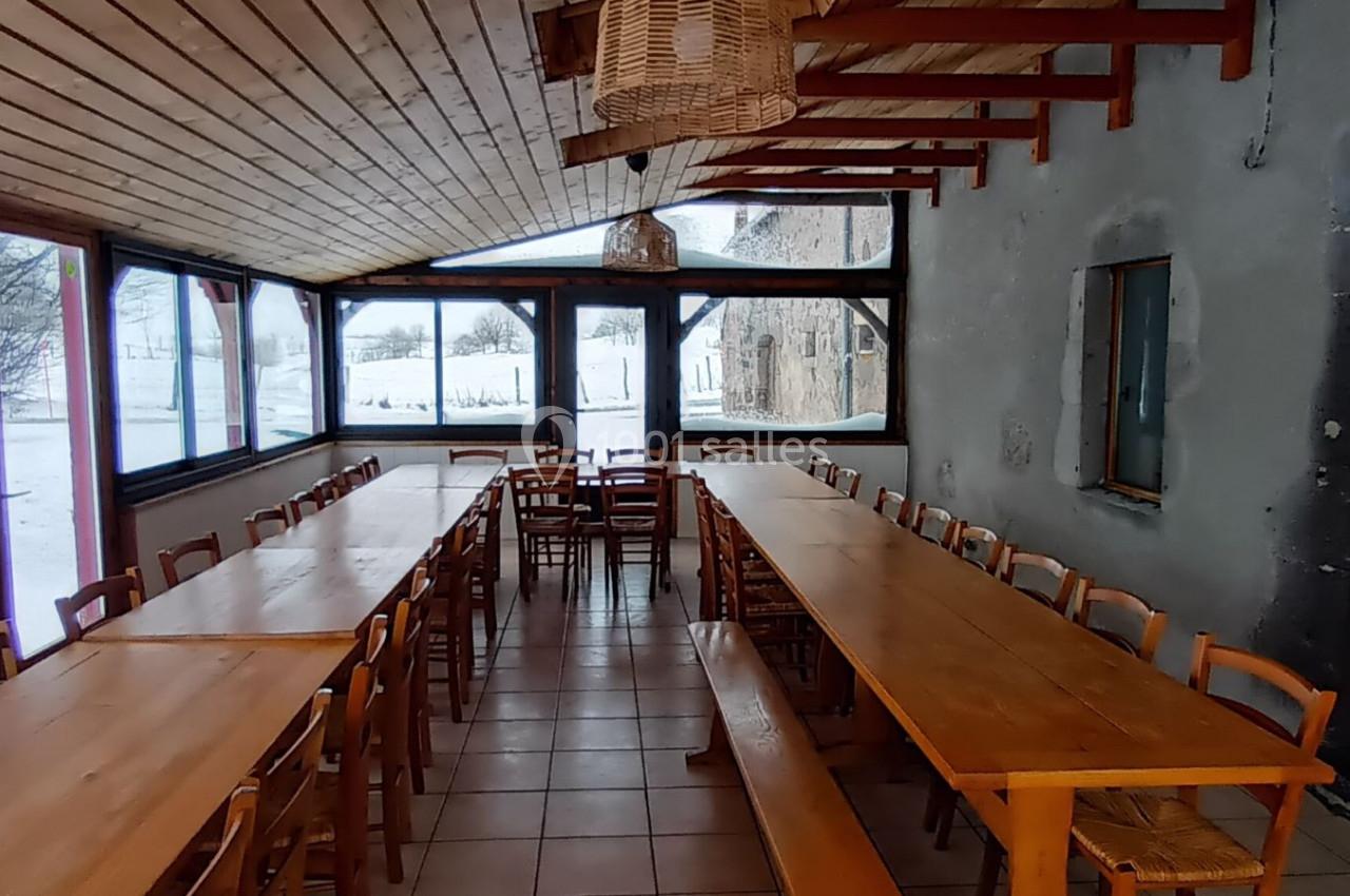 Salle à manger lumineuse avec de longues tables en bois, des chaises assorties et de grandes fenêtres donnant sur un paysage…