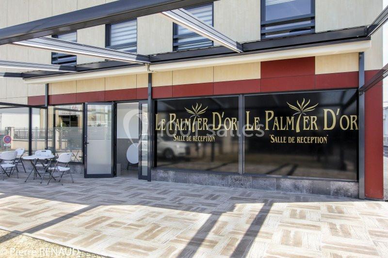 Façade d'une salle de réception avec terrasse aménagée et enseigne ’Le Palmier d'Or’.