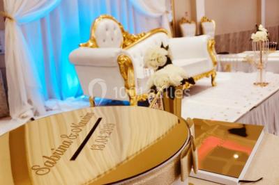 Salle de réception décorée avec une table dressée, un centre de table floral et une arche fleurie en arrière-plan.