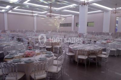 Salle de réception décorée avec une table dressée, un centre de table floral et une arche fleurie en arrière-plan.