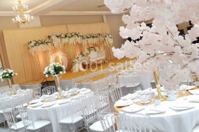 Salle de réception décorée avec une table dressée, un centre de table floral et une arche fleurie en arrière-plan.