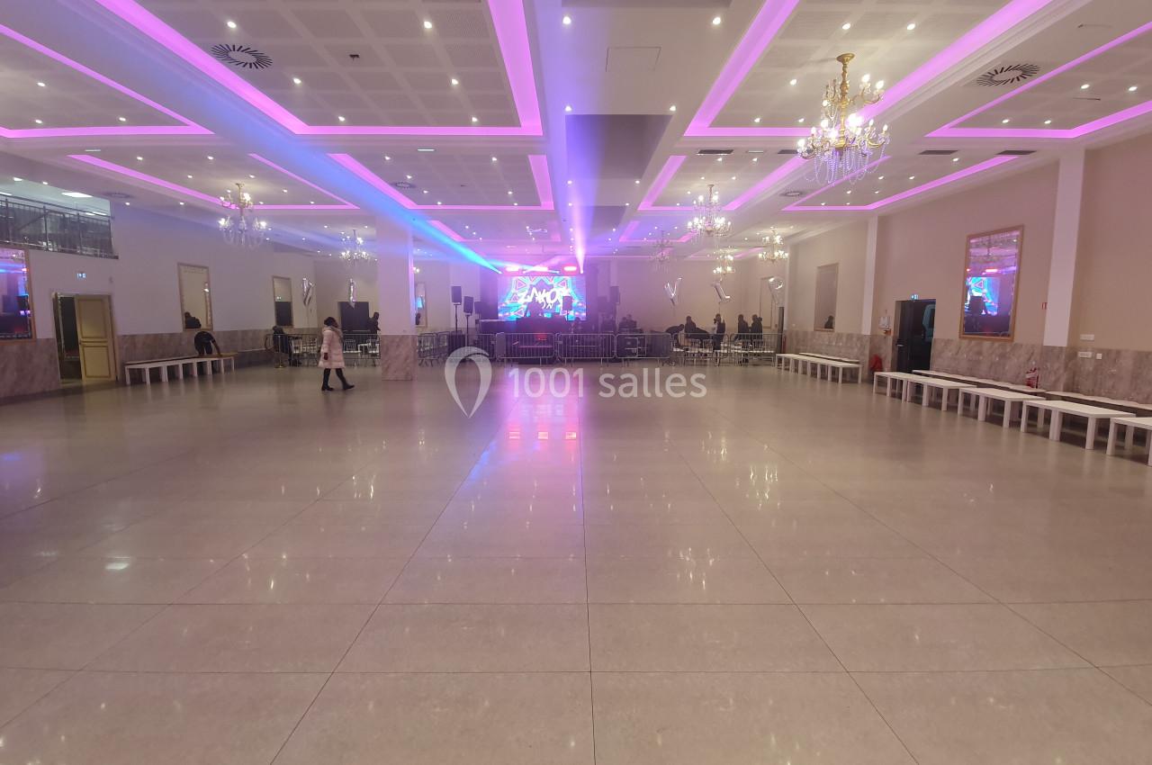 Salle spacieuse avec sol en carrelage, éclairage néon rose et blanc, scène au fond et quelques personnes présentes.