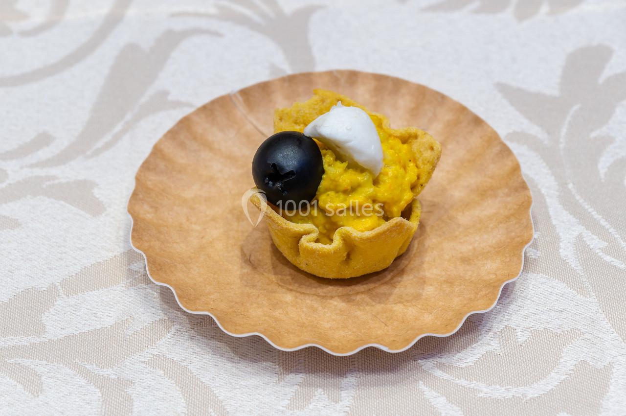 Tartelette garnie de purée de légumes jaunes, décorée d'une olive noire et d'une touche de crème blanche.