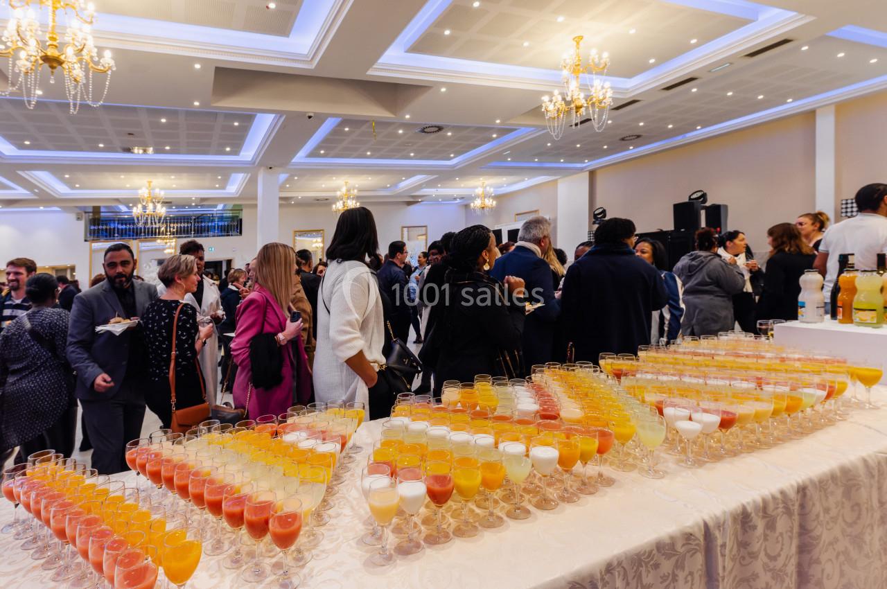 Salle de réception animée avec des invités debout près d'une table garnie de verres de jus colorés.