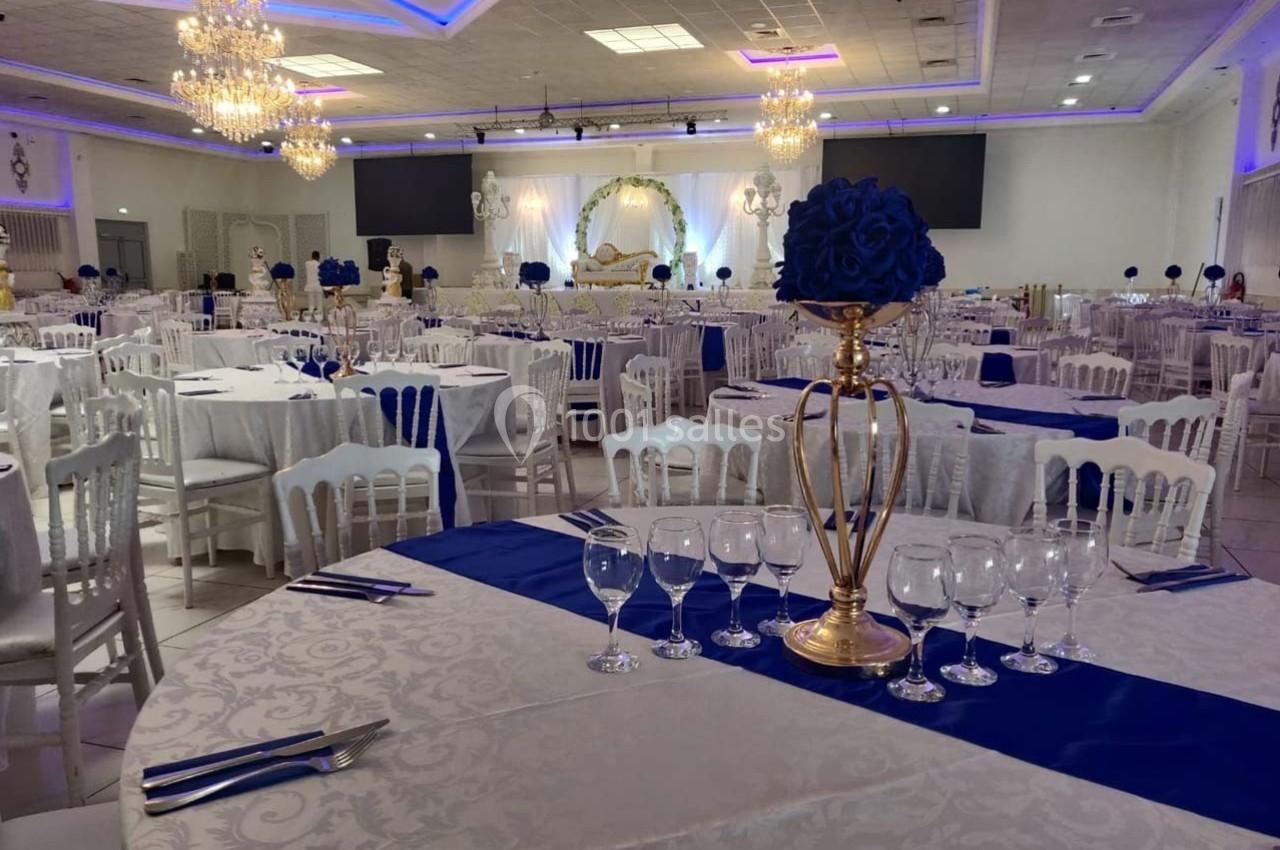 Salle de réception élégante avec tables dressées, nappes blanches, chemins de table bleus et décorations florales.