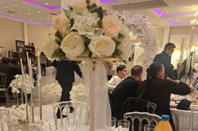 Salle de réception décorée avec une table dressée, un centre de table floral et une arche fleurie en arrière-plan.