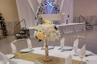 Salle de réception décorée avec une table dressée, un centre de table floral et une arche fleurie en arrière-plan.