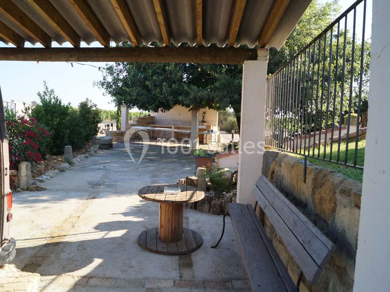 Cour extérieure avec banc en bois, bobine en bois utilisée comme table, arbres et végétation en arrière-plan.