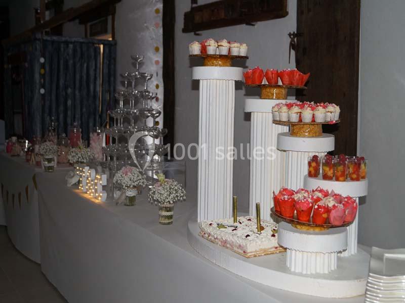 Table de desserts décorée avec des gâteaux, verrines et fleurs, accompagnée d'une fontaine à champagne.