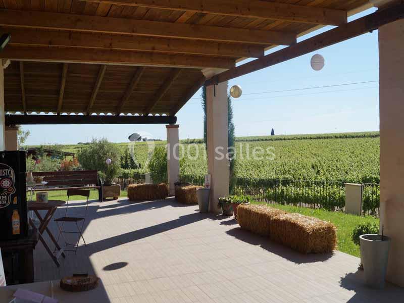 Terrasse couverte avec vue sur des vignes, décorée de bottes de paille et lanternes suspendues.