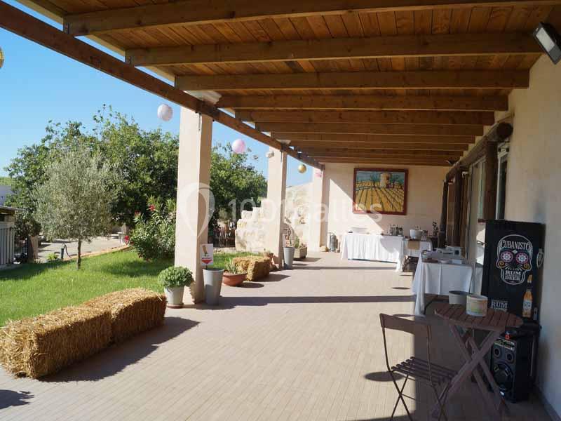 Terrasse couverte avec mobilier en bois, ballons suspendus, bottes de paille et vue sur un jardin ensoleillé.