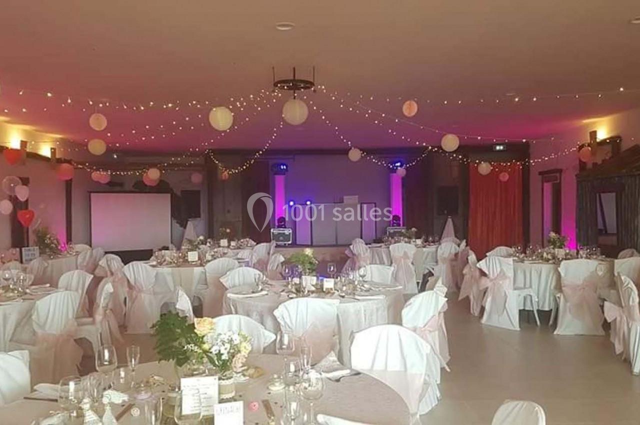 Salle de réception décorée avec des tables dressées, des chaises couvertes de housses blanches et des guirlandes lumineuses…