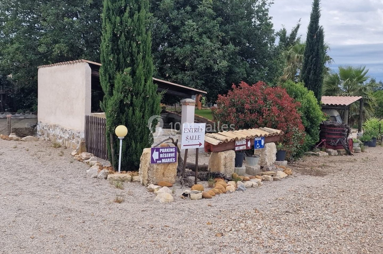 Entrée d'un domaine rural avec panneaux directionnels, végétation méditerranéenne et chemin en gravier.