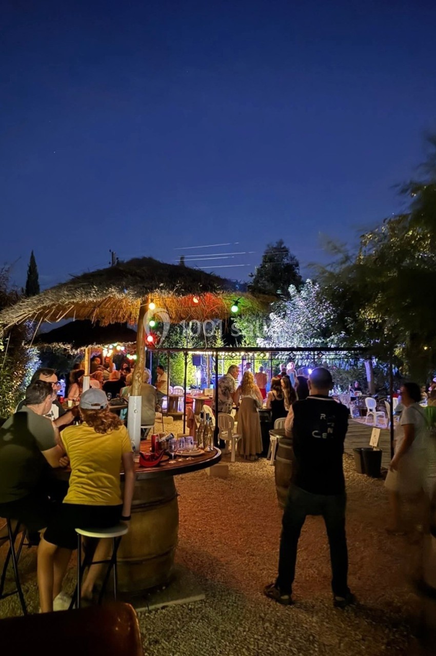 Personnes rassemblées dans un bar extérieur éclairé par des guirlandes lumineuses sous un ciel nocturne.