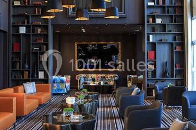 Chambre d'hôtel lumineuse avec lit double, bureau bleu, fauteuil, télévision et balcon offrant une vue sur l'extérieur.